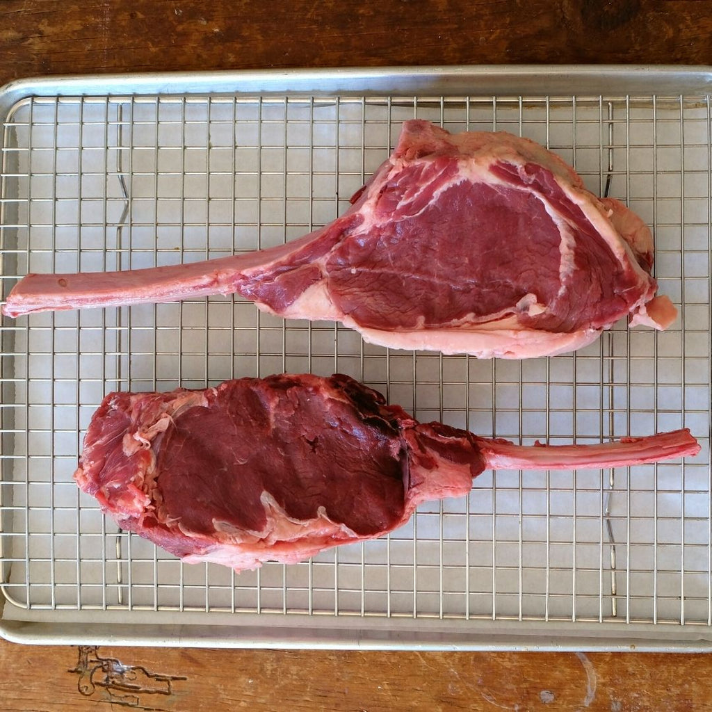 Two raw Bison Tomahawk steaks on a cooking rack.