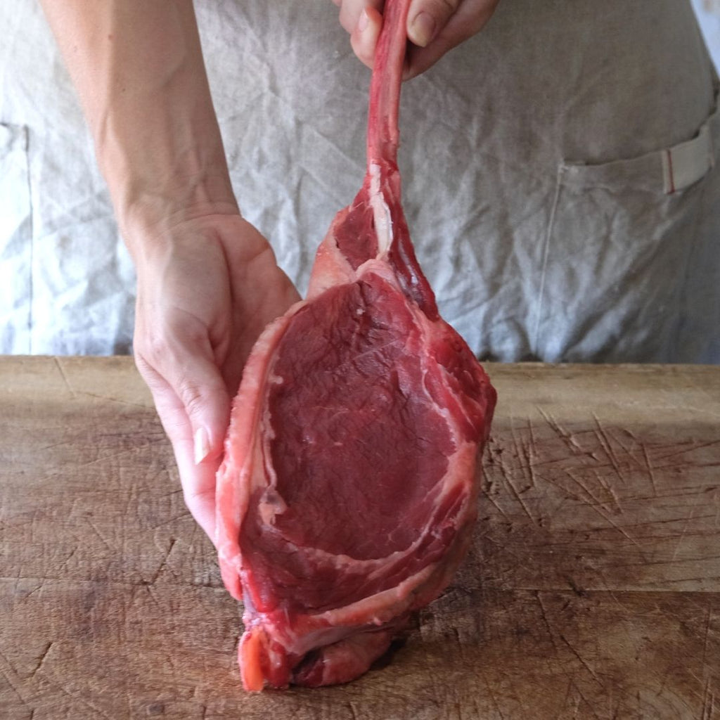 Woman holding up a raw bison tomahawk steak by the bone against a counter.