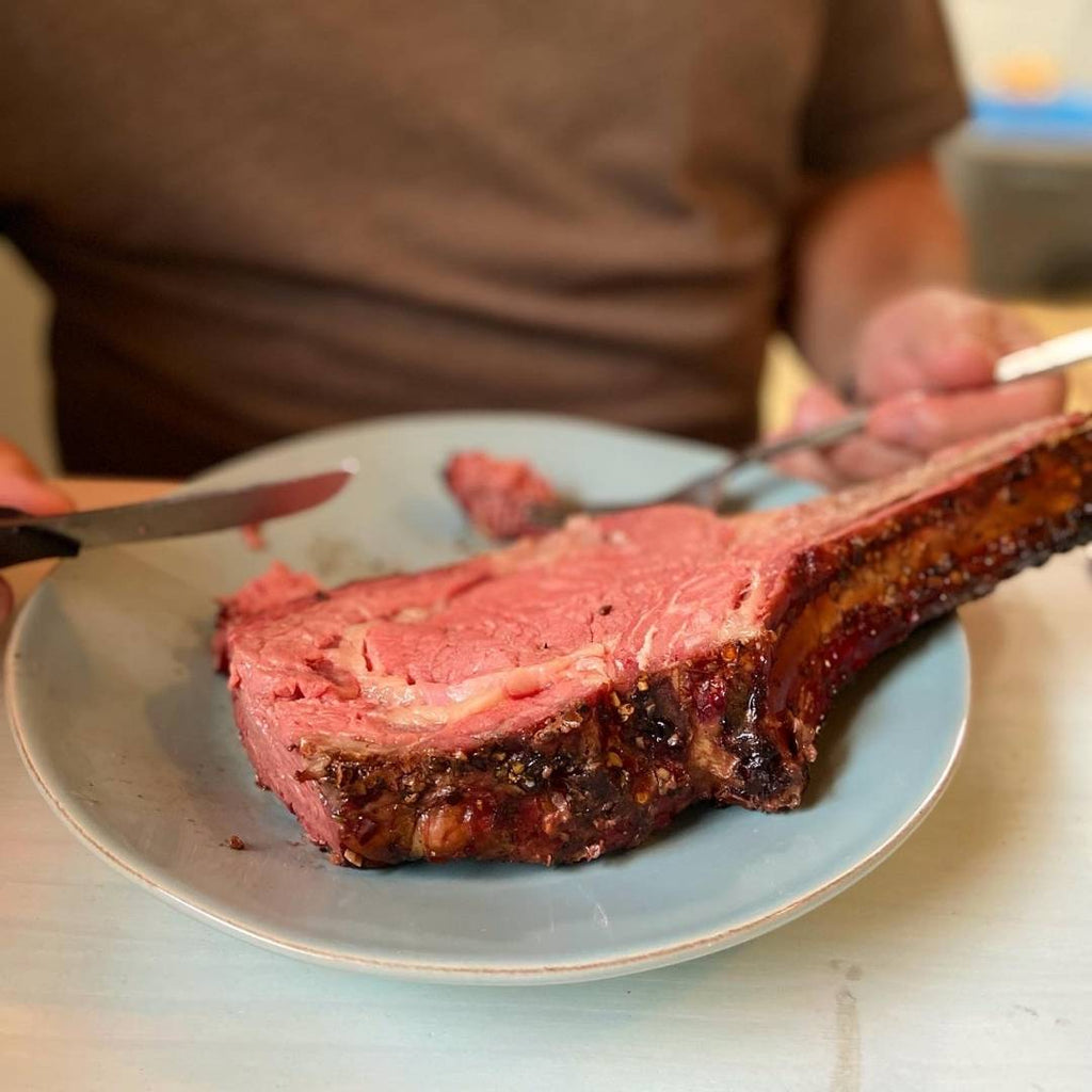 A giant slice of bison prime rib on a plate, ready to eat on table in front of man.
