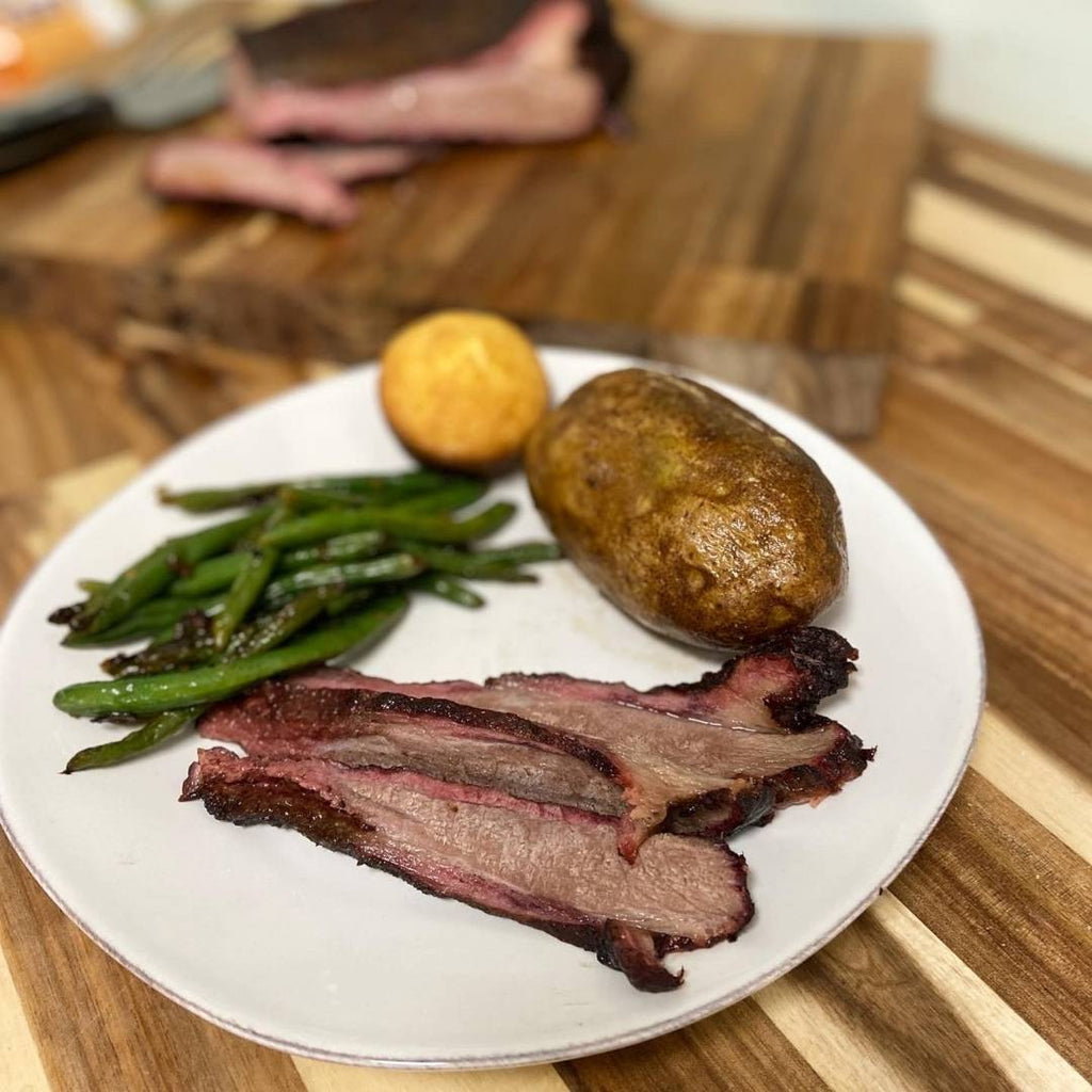 Sliced bison brisket on plate with green beans, baked potato and corn bread muffin.