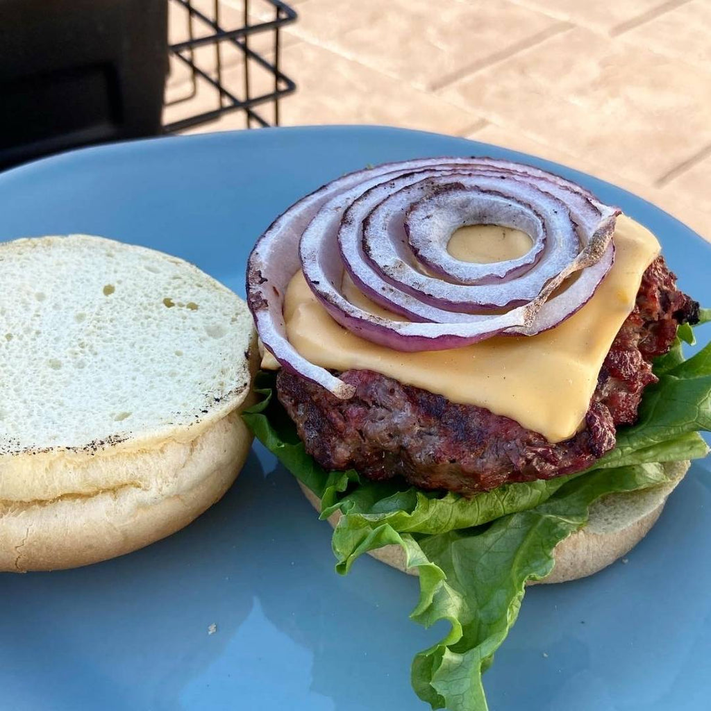 Bison Burger on a bun with red onion, cheese and lettuce.