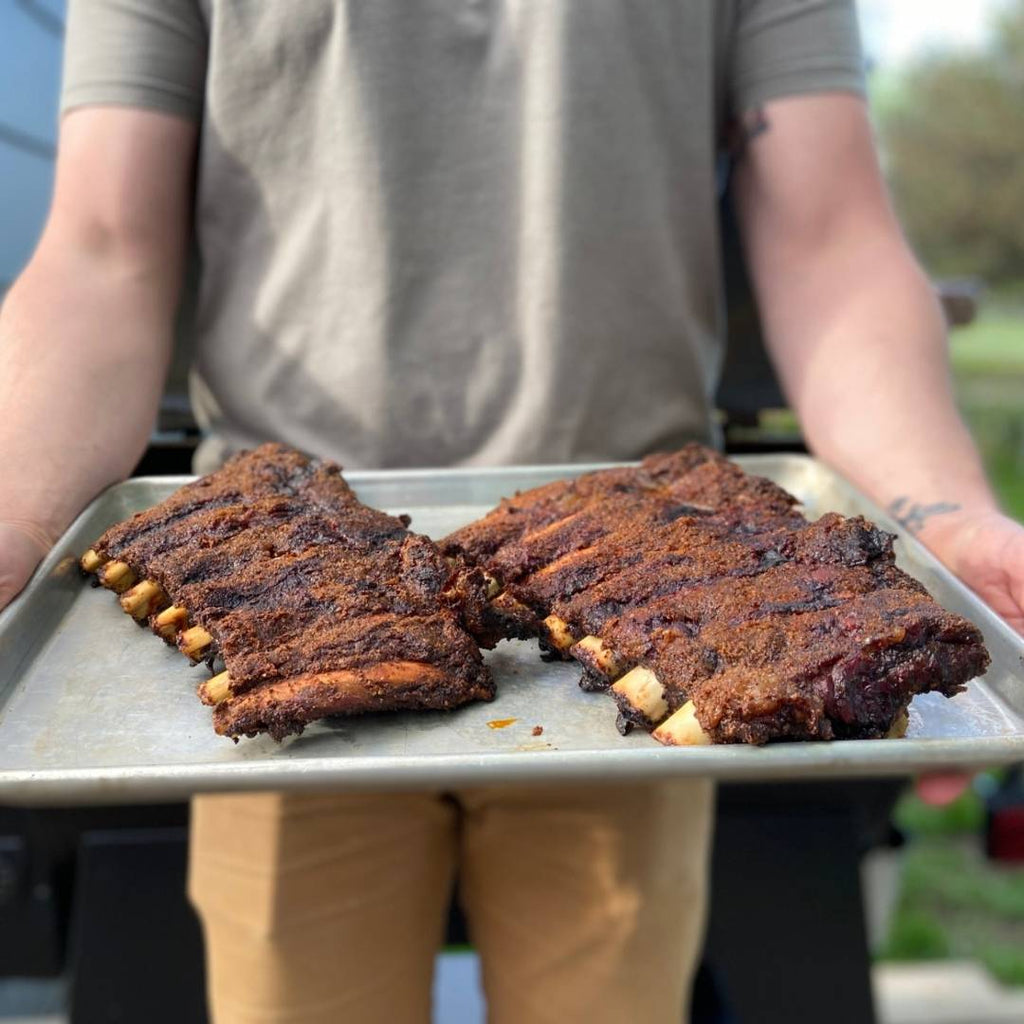 Man holding a tray of cooked bison back ribs.