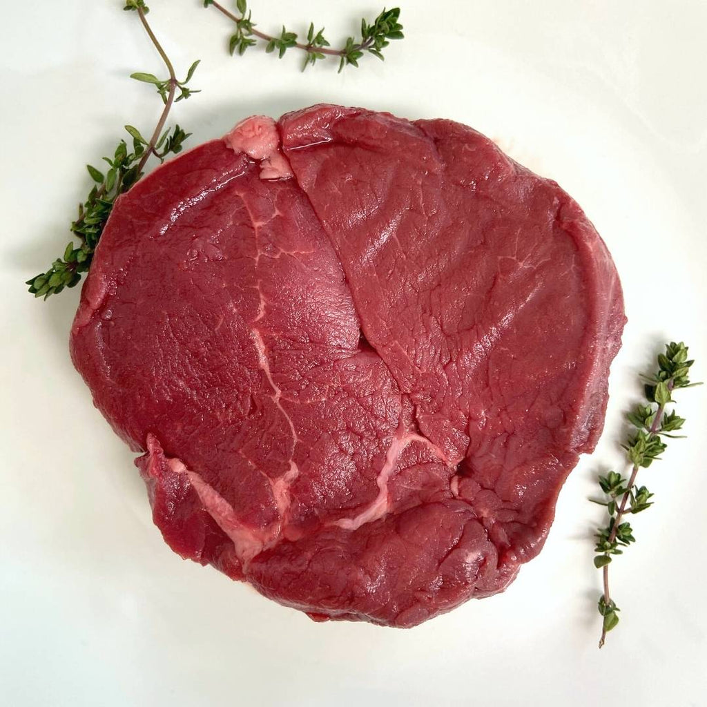 Raw bison filet mignon on white plate with thyme sprigs.