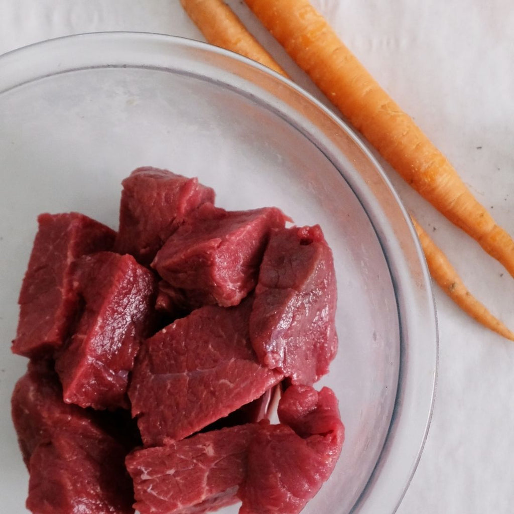 Cut up bison roast pieces in bowl next to carrots.