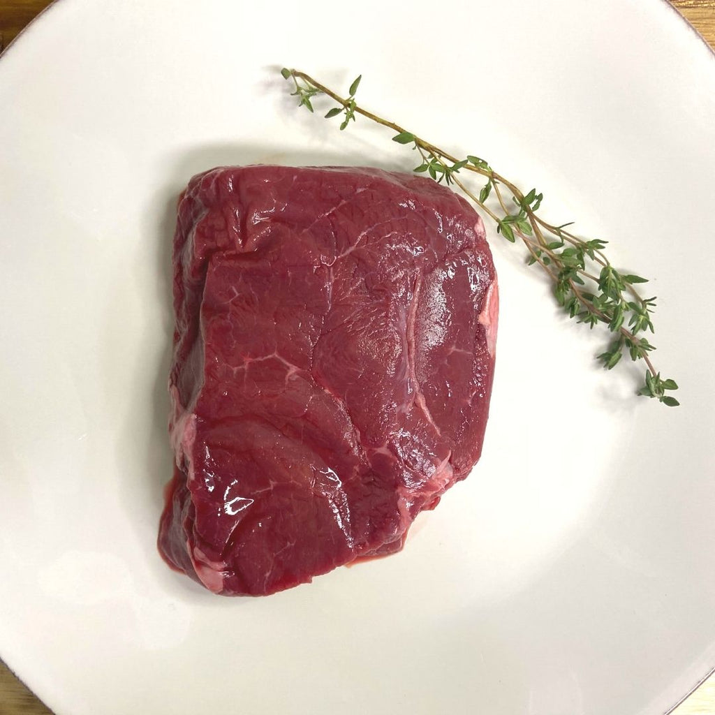 Bison Top Sirloin, raw on white plate with sprig of thyme.
