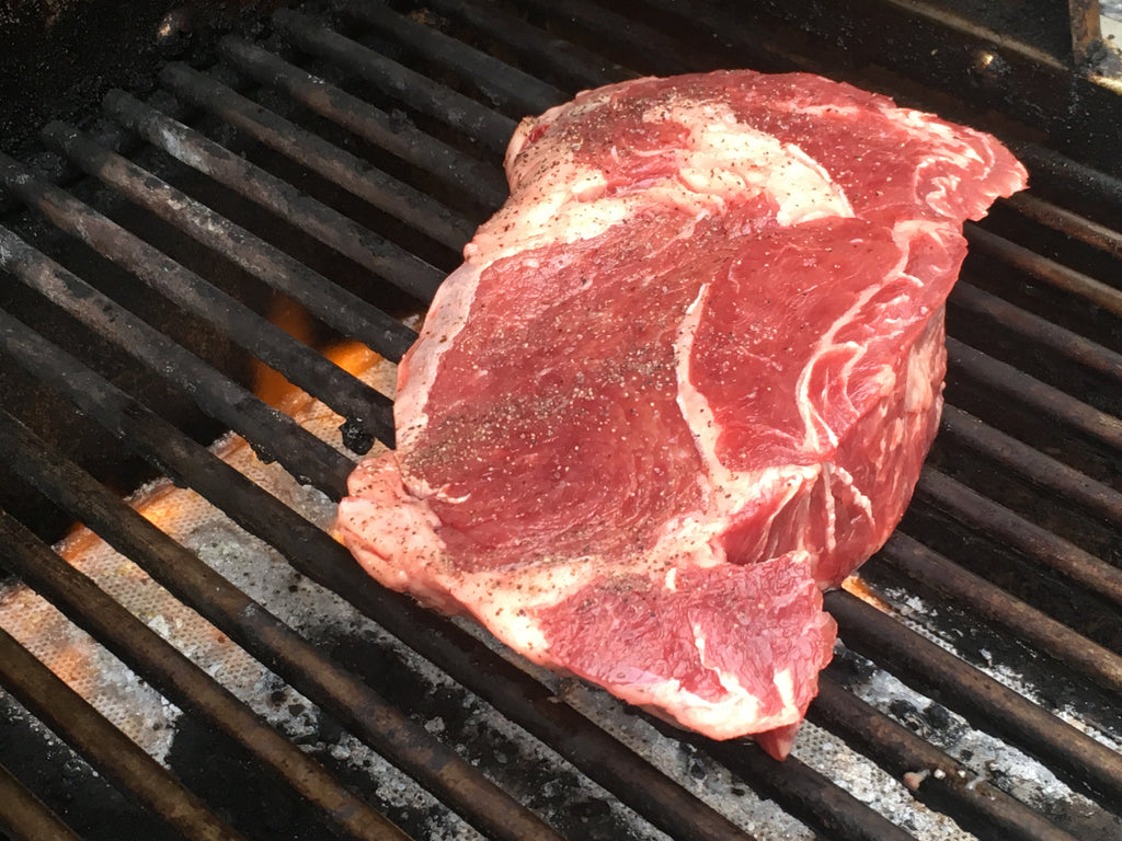 A well-marbled Bison Ribeye Steak cooking on the grill.