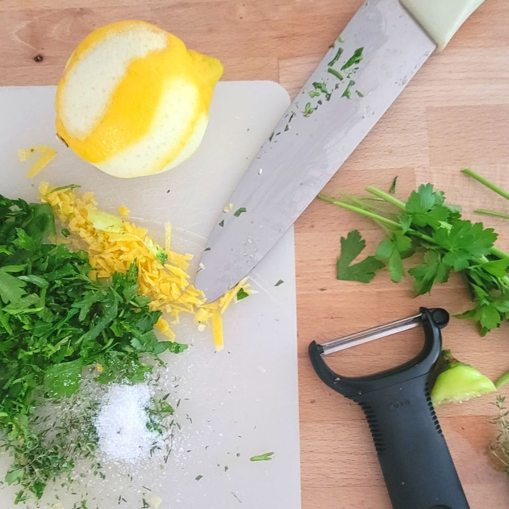 zested lemon on counter with chopped parsley, seasonings, knife and peeler.