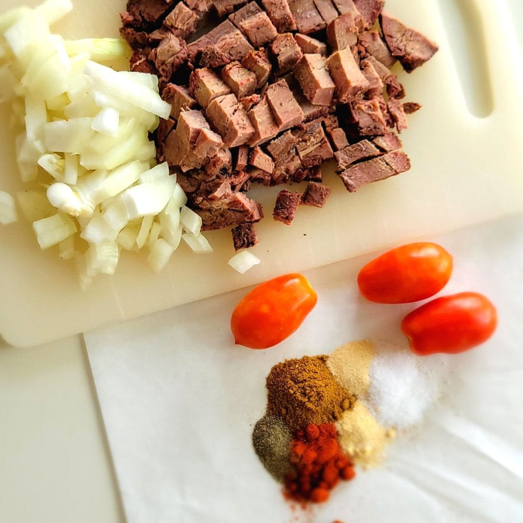 chopped onions and steak on cutting board with tomatoes and spices below.
