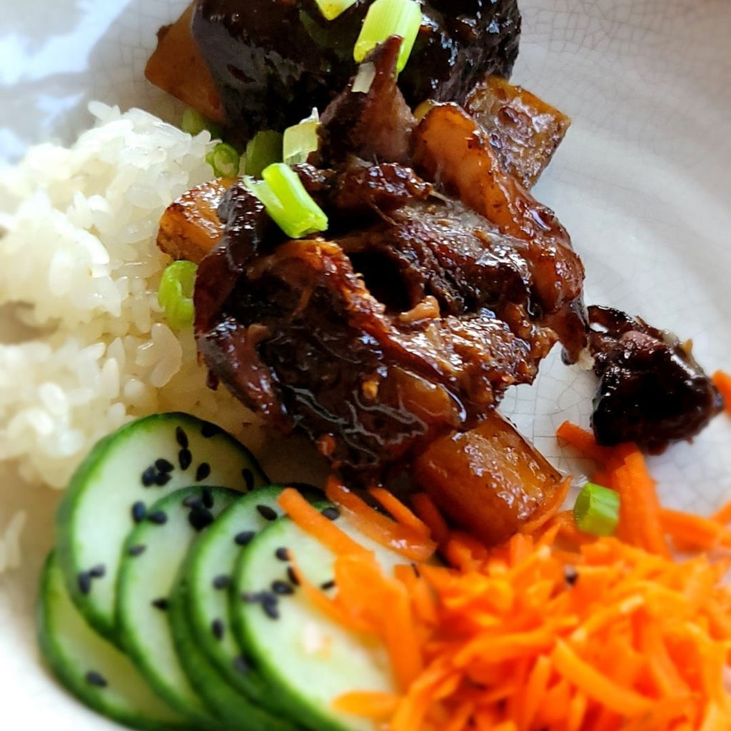 Cooked bison short ribs on a plate with rice, cucumber and shredded carrots.