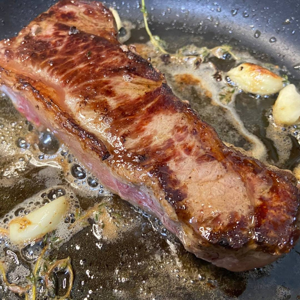 Bison NY Strip steak cooking in pan.