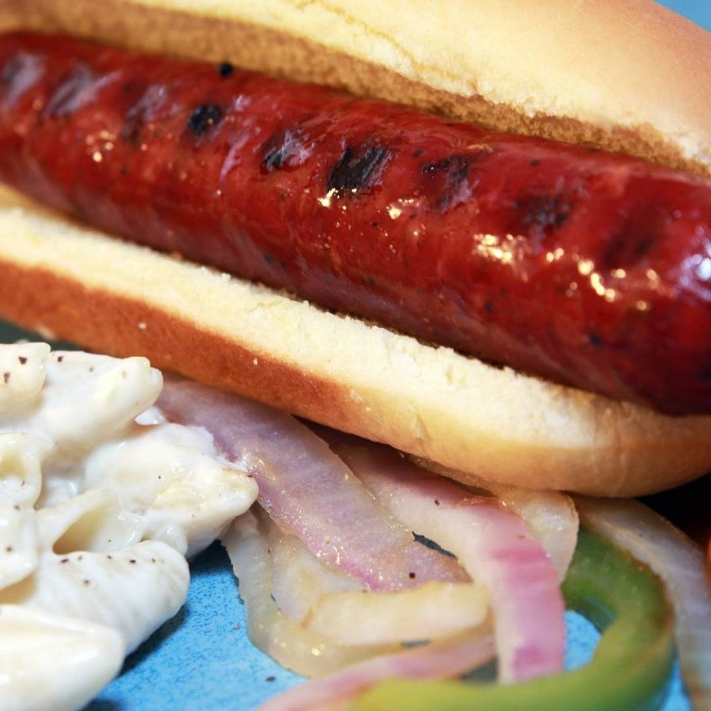 Elk Sausage in bun with onions and pasta salad on plate.