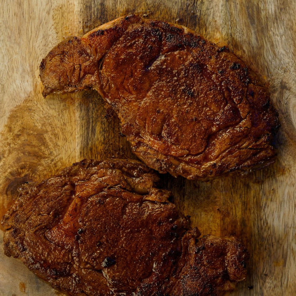 2 cooked bison ribeye steaks on a cutting board.