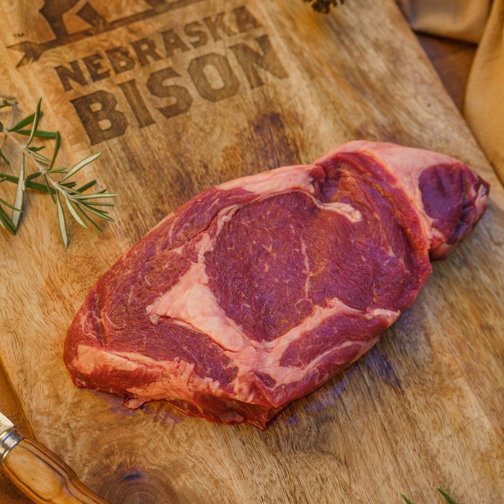 Raw bison steak on a wood cutting board with Nebraska Bison logo burned into it.